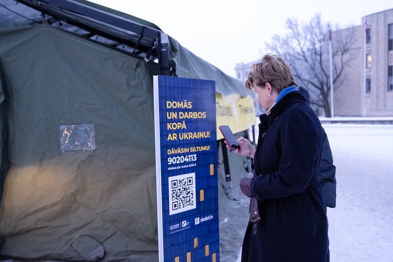  Baiba Braže scans the QR code of the "Ziedot.lv" campaign "Warmth for Ukraine from Latvia" at the Unbreakable Point tent