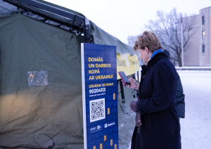Baiba Braže pie Nesalaužamības punkta telts skanē "Ziedot.lv" akcijas "Siltums Ukrainai no Latvijas" QR kodu