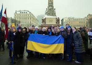 Diplomātiskā kora dalībnieki pie brīvības pieminekļa turot rokās Ukrainas karogu